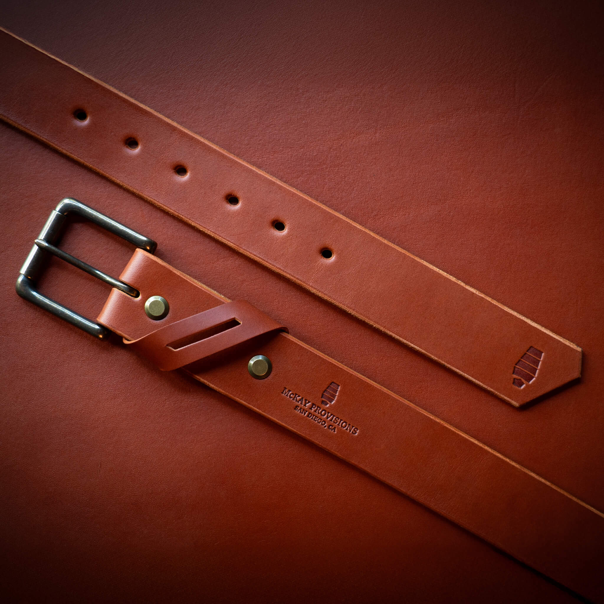 Chestnut leather belt with a brass buckle on a chestnut leather background