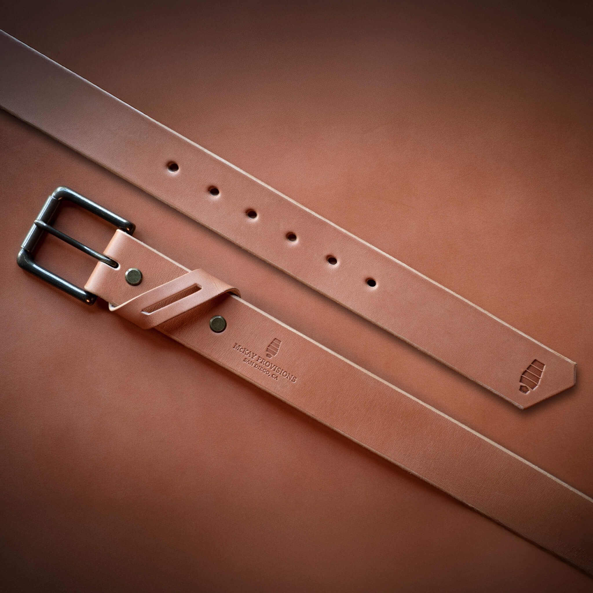 Tan leather belt with a brass buckle on a tan leather background