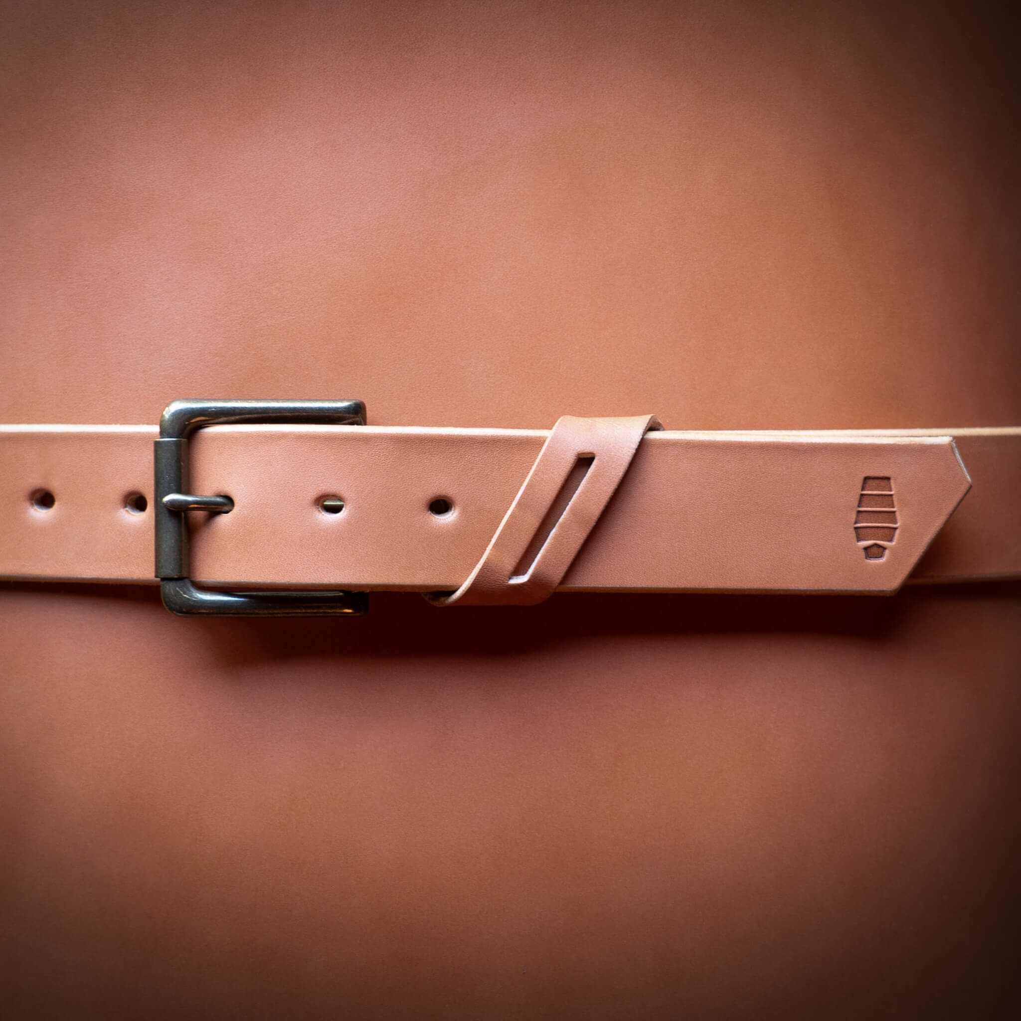 Tan leather belt with a brass buckle wrapped around a rolled up leather hide.