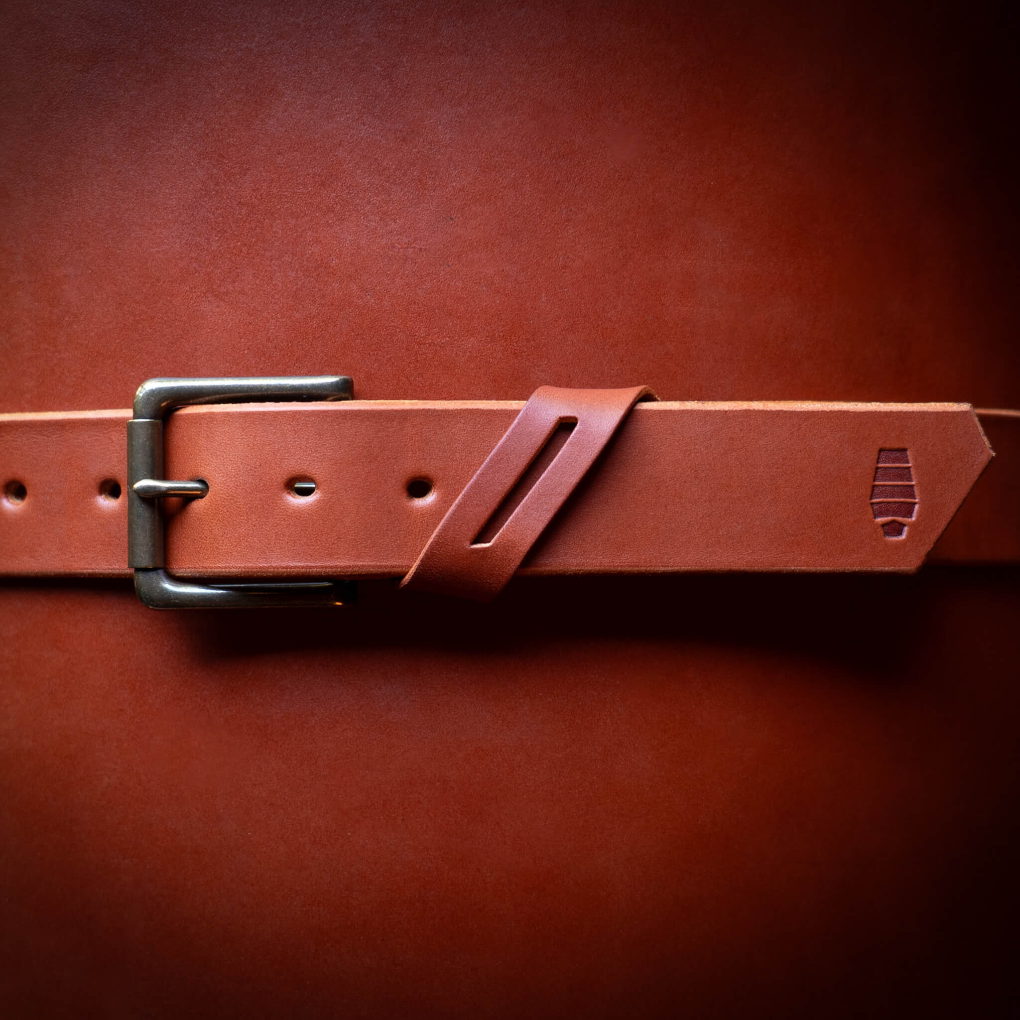 Chestnut leather belt with a brass buckle wrapped around a rolled up leather hide.