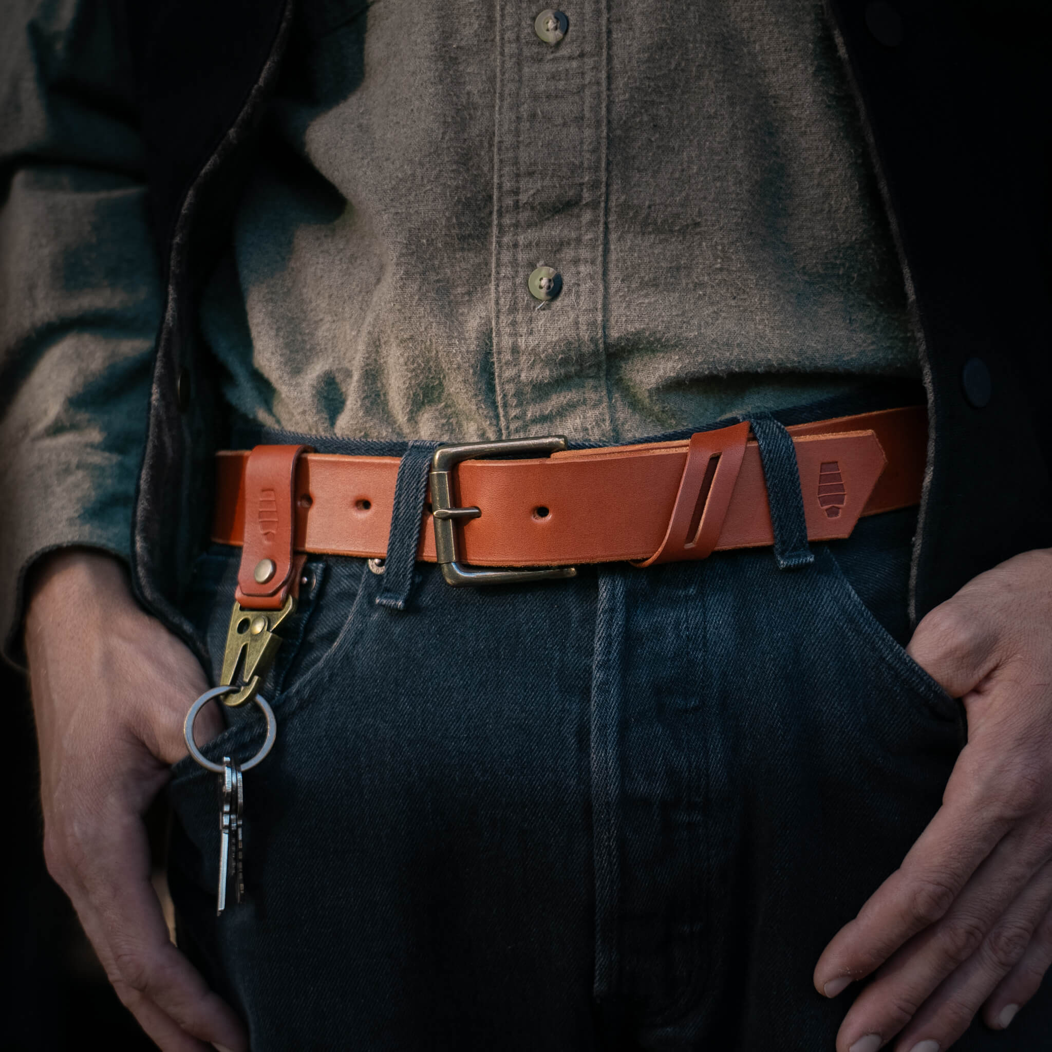 Person wearing a brown leather belt with a keychain, dark shirt, and jeans.