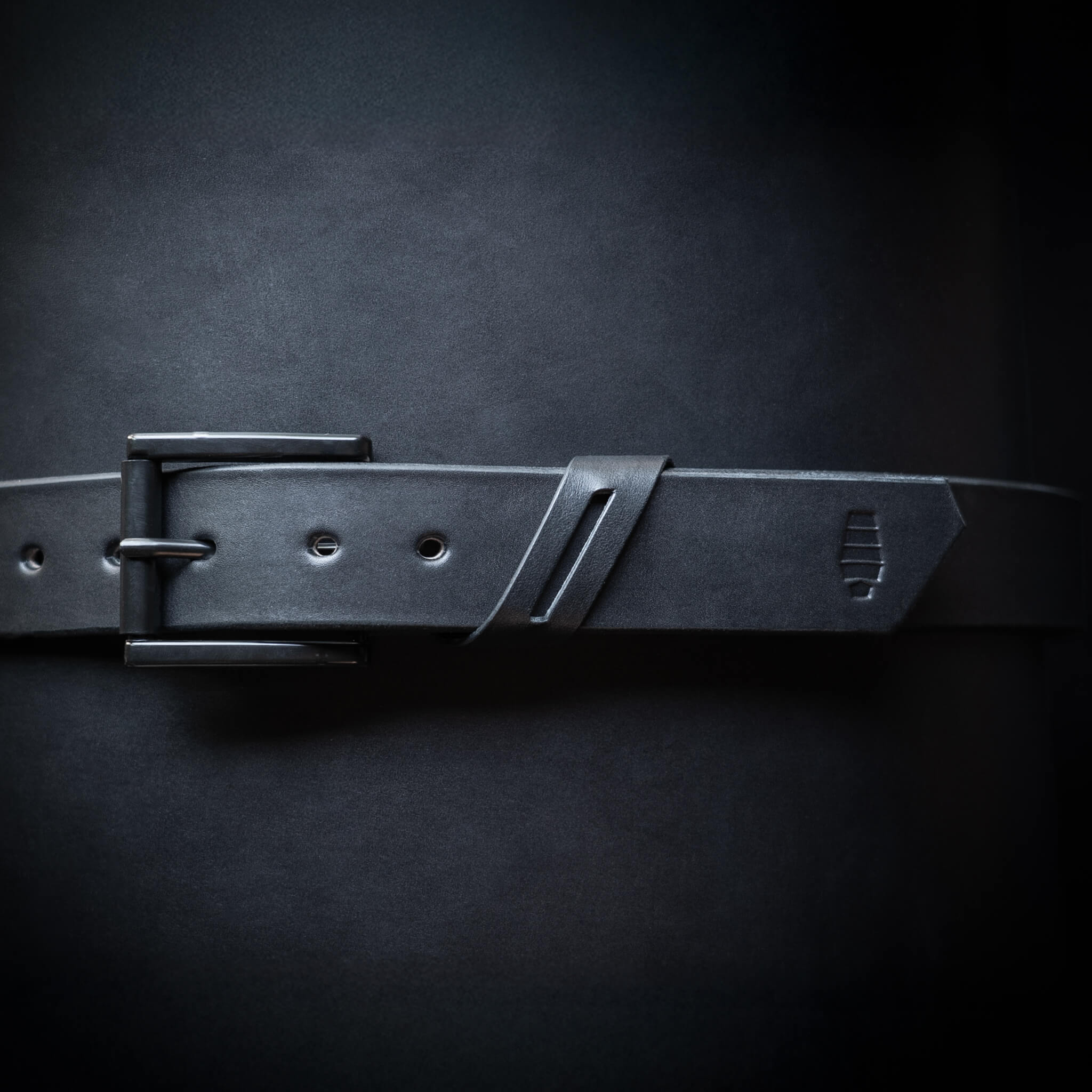 Black leather belt with a black buckle wrapped around a rolled up leather hide.