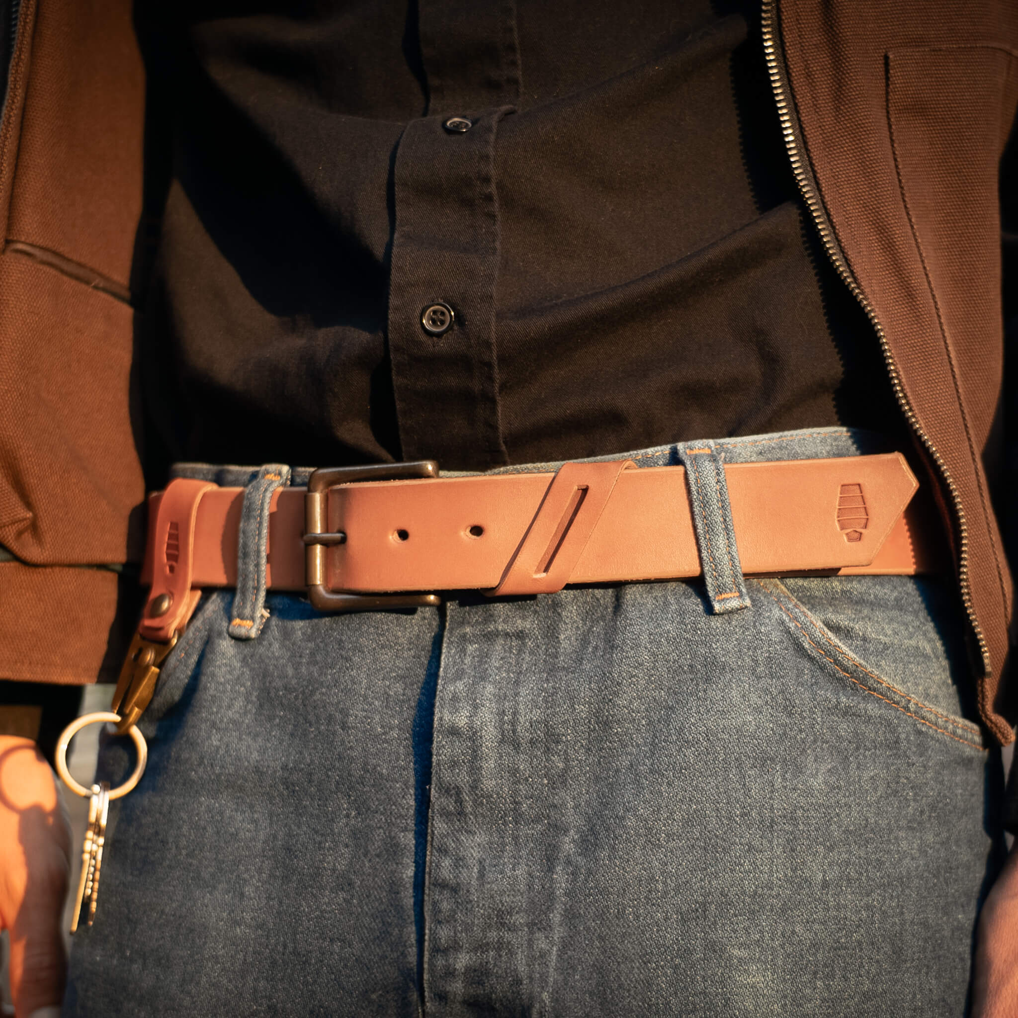 Person wearing a tan leather belt with a matching keychain attached, standing against a neutral background.