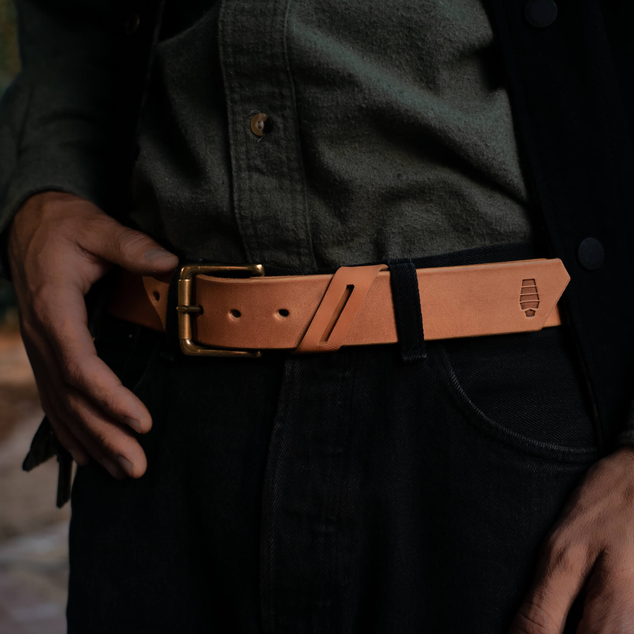 Person wearing a tan leather belt with a brass buckle.