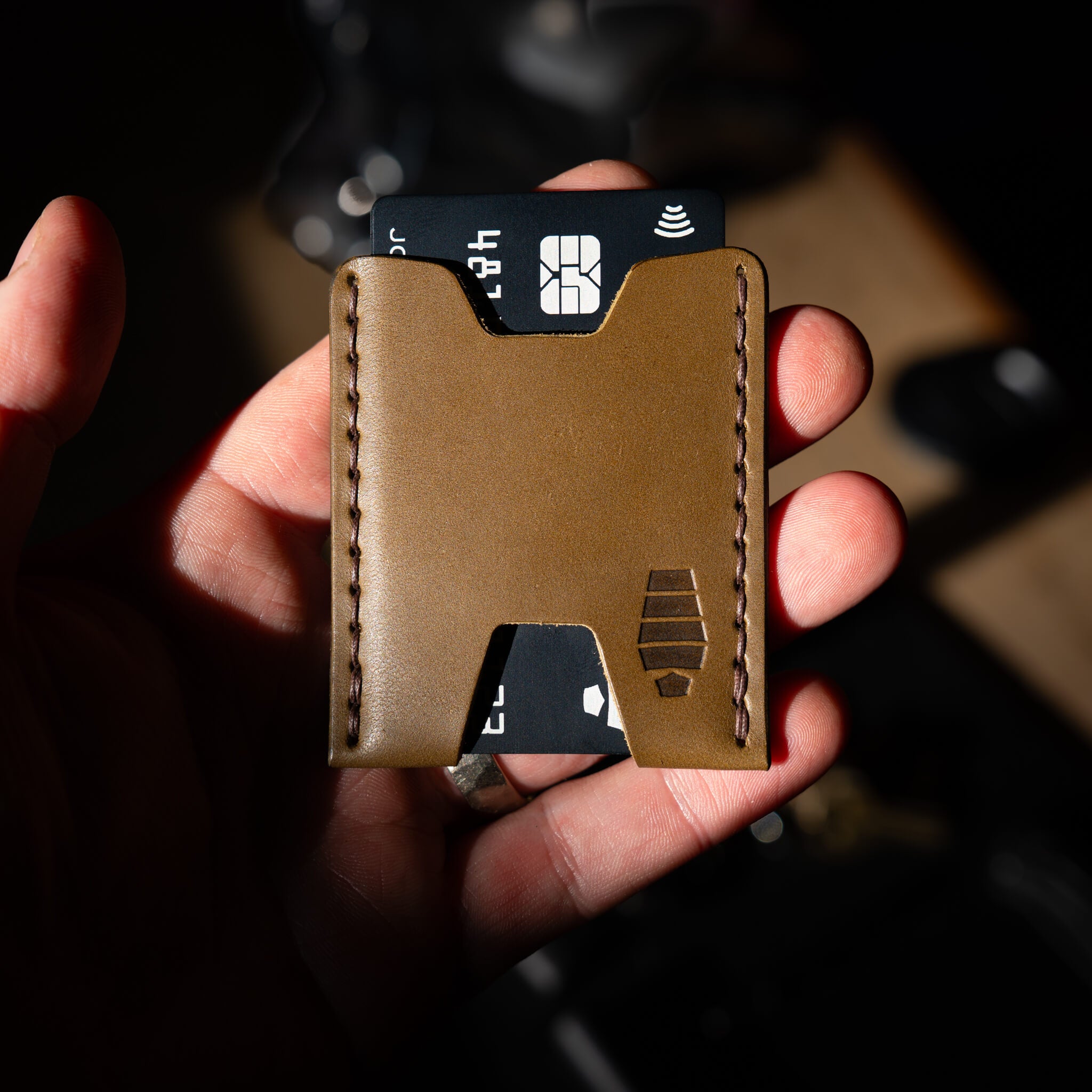 Ulysses slim leather card wallet in Ranger green color, held in hand, showing hand-stitched Maine thread in detail and front-pocket scale.