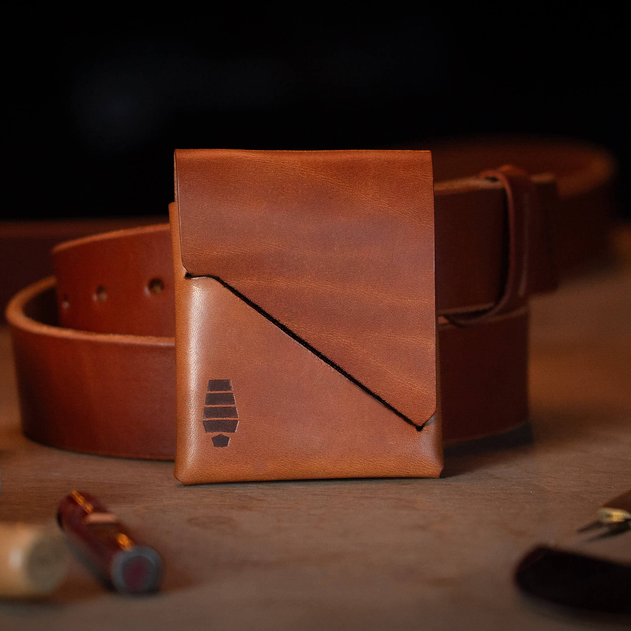 Voyager Canyon Brown minimalist wallet styled with Mainstay leather belt on wood surface showing handcrafted everyday carry aesthetic