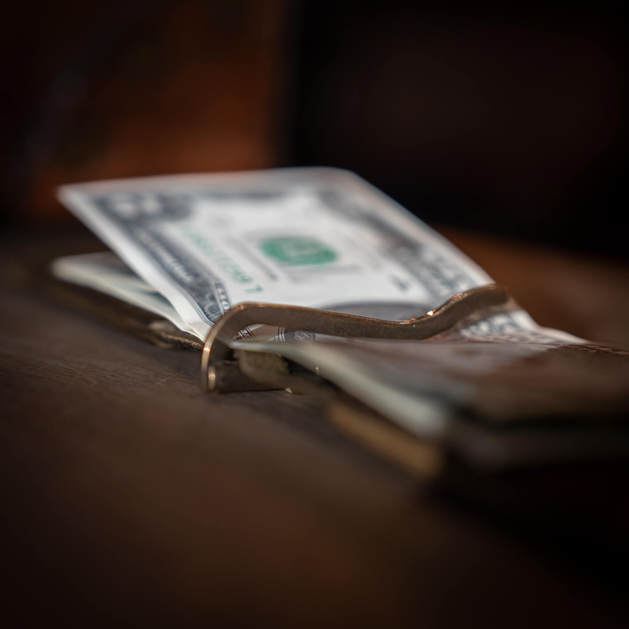 Close up of solid brass spring-action money clip closed holding cash in the Windward wallet.
