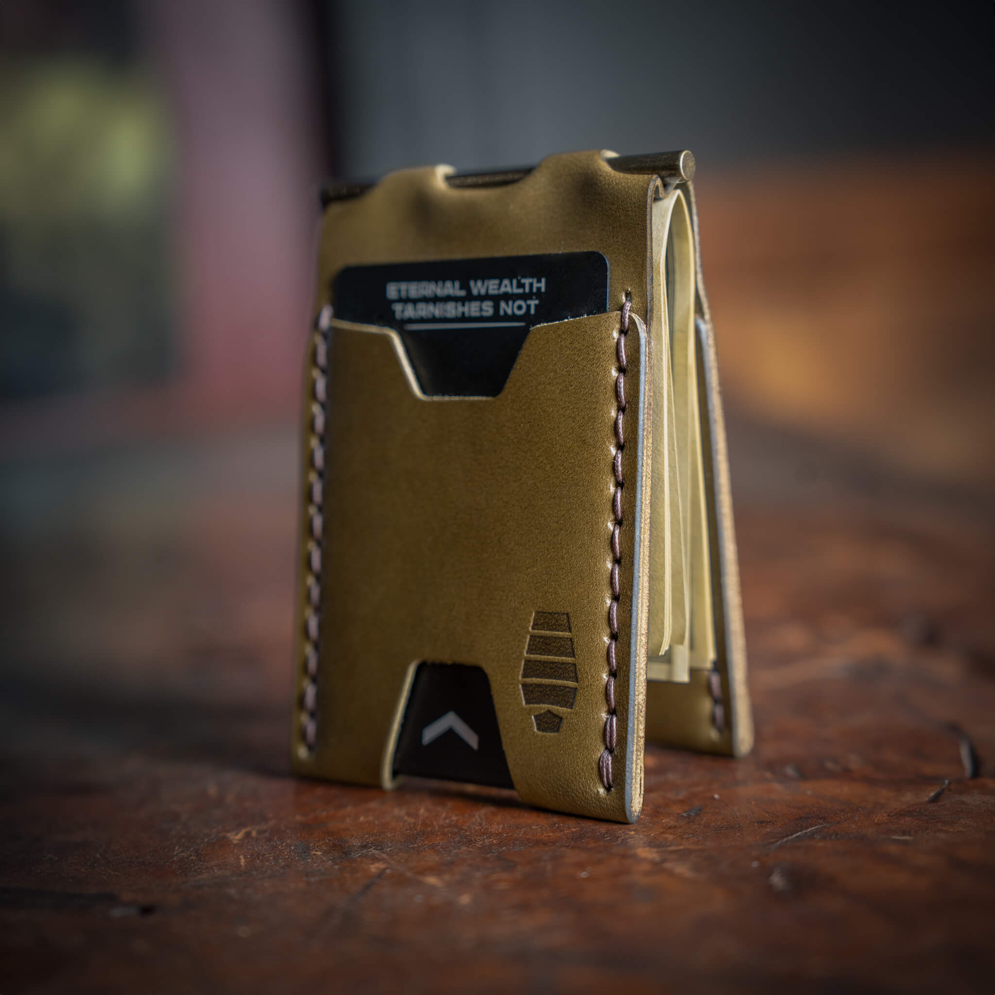 Windward minimalist leather wallet in ranger green standing up on a rustic surface, showing hand stitched thread details.