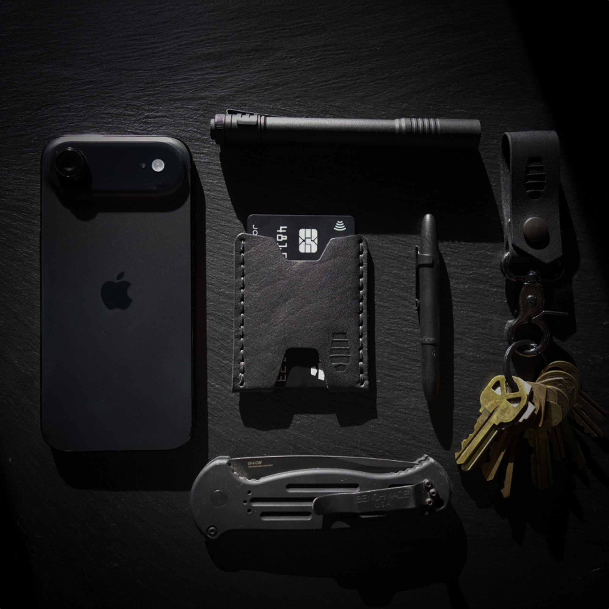 Black Ulysses minimalist leather wallet in everyday carry layout with keys, phone, and pocket tools.