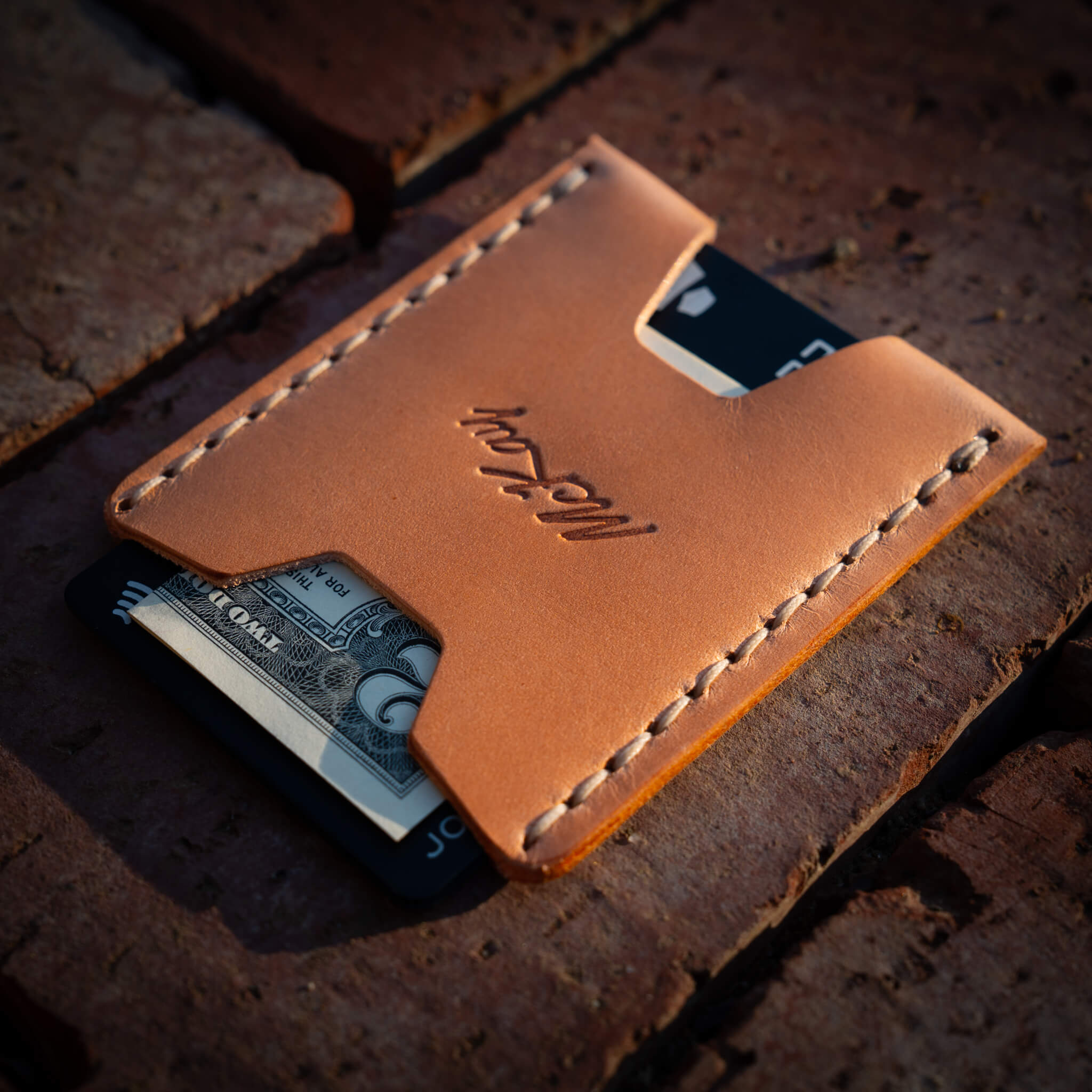 Back of Ulysses wallet with McKay Provisions logo and hand-stitched detailing, holding folded up cash.
