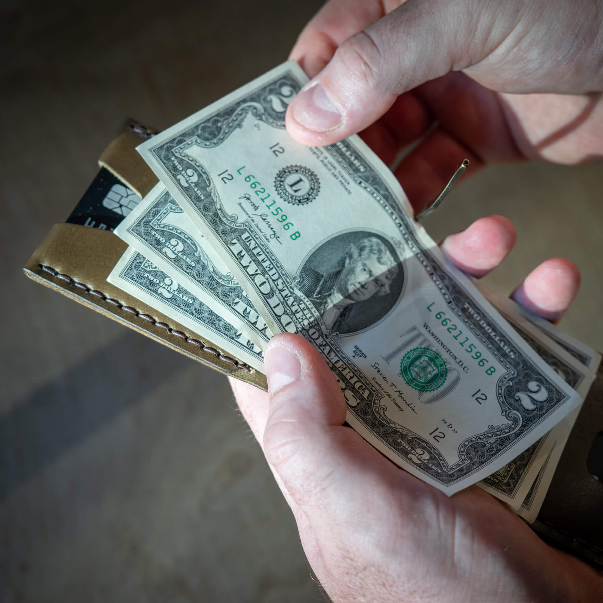 Hand retrieving cash from Windward Canyon leather wallet with open brass money clip