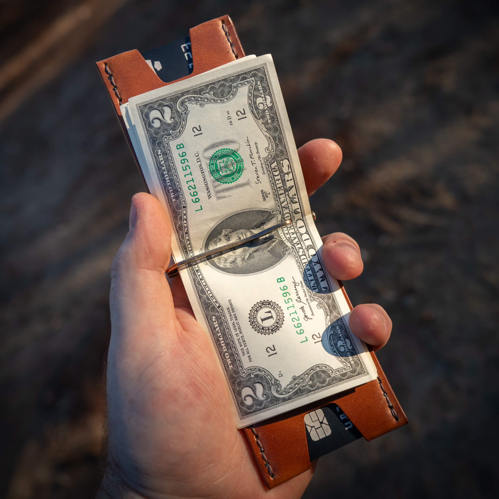 Windward leather wallet being held open in hand with the money clip and cash visible.
