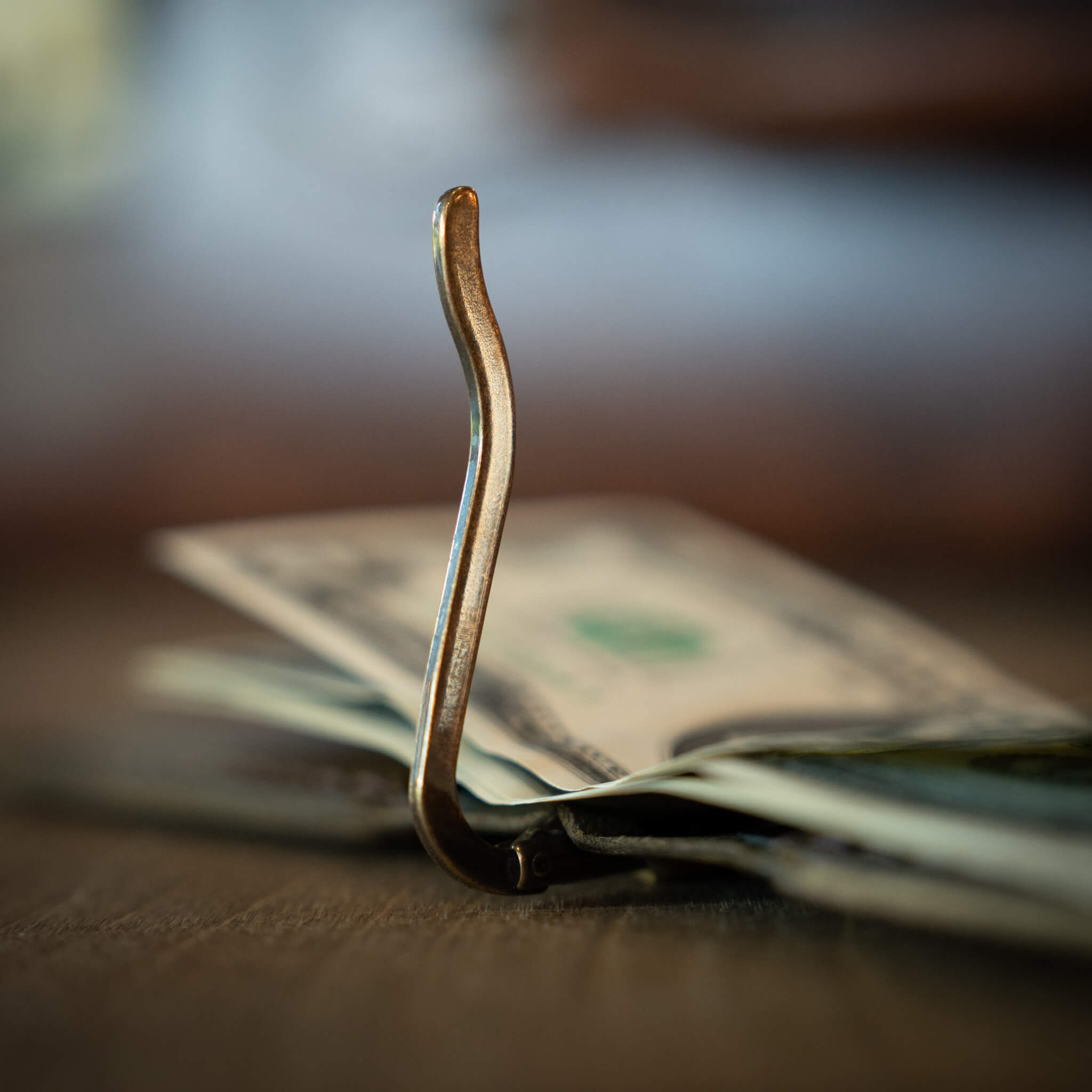 Close up of solid brass spring-action money clip open holding cash